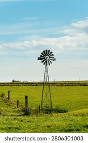 A rustic windmill stands in a green field under a clear blue sky, evoking a serene rural landscape.