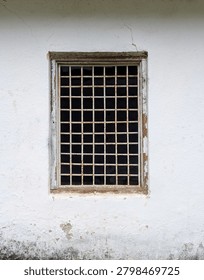 Rustic window with rusty metal security grate on white weathered wall	
