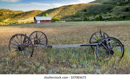 Rustic wood wagon sits in a farmers field with a barn