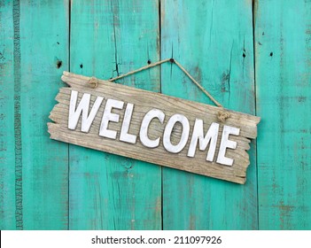 Rustic wood welcome sign hanging on weathered antique teal blue door;  wooden sign with painted background