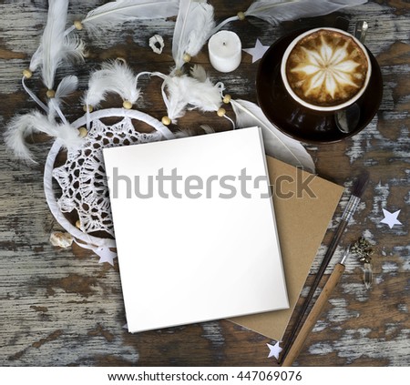 Rustic wooden background with boho chic style decorations: dreamctcher, cup of cappuccino, notebook and paper stars. Copy space for text. Natural, rustic, ethnic or hipster vintage mock up. Top view. 