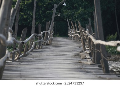 Rustic wooden bridge made of planks, with bamboo railings, across river. Unstable bridge in close-up against, background dark jungle tropical forest. Vintage country winding bridge.  - Powered by Shutterstock