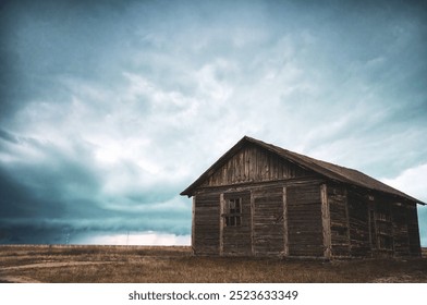 Rustic wooden cabin sits under a dramatic cloudy sky, surrounded by open countryside, with weathered textures and natural tones - Powered by Shutterstock