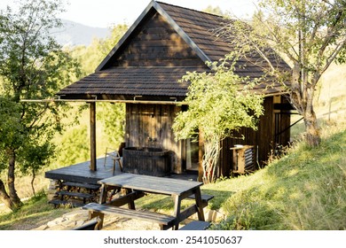 Rustic wooden cabin surrounded by nature, featuring a cozy porch with an outdoor bathtub and a picnic table. Perfect spot for a peaceful countryside escape - Powered by Shutterstock