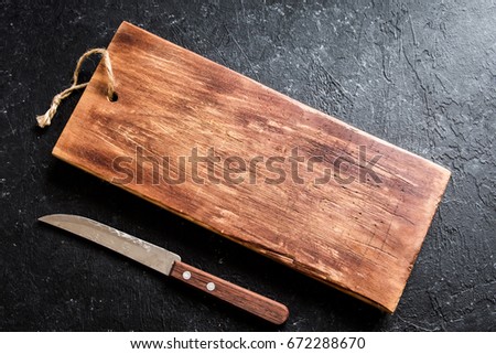 Rustic wooden cutting board and knive on black stone background close up - rustic empty copy space for text, design element