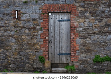 A rustic wooden door set within a weathered stone and brick wall, surrounded by patches of greenery. The image captures a vintage, historic atmosphere highlighting age and architectural charm - Powered by Shutterstock