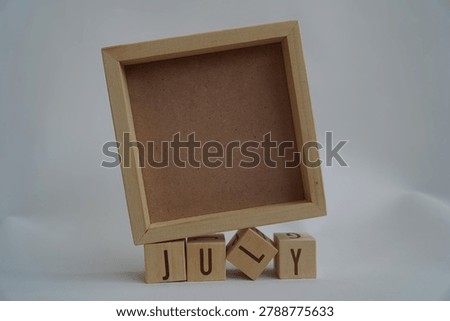 Rustic Wooden Empty Square Frame Resting on Jumbled July Wooden Letter Blocks