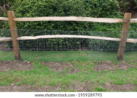 Rustic wooden fence with chicken wire for added protection in front of bush