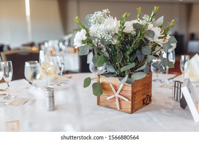 Rustic Wooden Floral Box With White And Green Eucalyptus Arrangement Decorated With Starfish On A White Quest Table. Wedding Centerpiece, Side View.