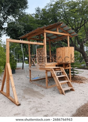 A rustic wooden playground structure rises on stilts with a sheltered roof, a swing, and timber stairs. Set in a sandy park area, surrounded by trees for a natural, playful space.