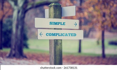 Rustic wooden sign in an autumn park with the words Simple - Complicated offering a choice of action and attitude with arrows pointing in opposite directions in a conceptual image.