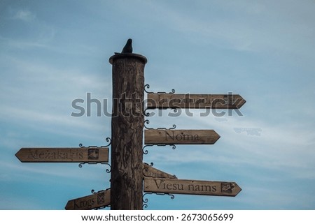 A rustic wooden signpost with multiple directional arrows in Latvian, pointing to local attractions or facilities such as “Informācija” (Information), “Noma” (Rental), “Viesu nams” (Guesthouse).