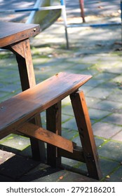 Rustic wooden table and bench seating arranged on an outdoor restaurant patio. Natural sunlight creates soft shadows across the stone pavement, conveying a calm and inviting atmosphere suitable for dining, hospitality, leisure, and outdoor lifestyle concepts.