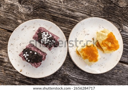  A rustic wooden table features two plates: one with sweet, purple dumplings topped with fruit sauce and sprinkles, and another with savory, light-colored dumplings dusted with breadcrumbs.