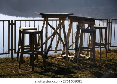 Rustic wooden table and stools made from birch branches beside a calm lakeside with metal railing