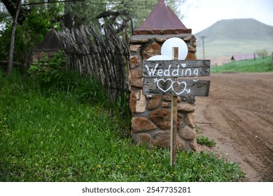 A rustic wooden wedding sign with heart decorations, directing guests down a dirt road toward a charming wedding venue, surrounded by natural greenery. - Powered by Shutterstock