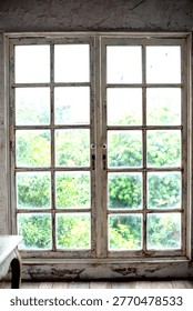 Rustic wooden window with multiple panes, offering a view of lush green foliage outside. The interior has a vintage, weathered charm.