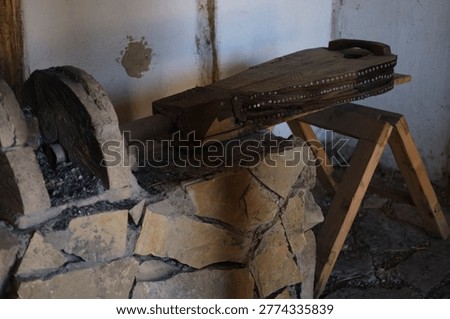 Rustic workshop interior with old wooden tool placed on stone surface supported by wooden sawhorse under natural light highlighting textured walls and traditional craftsmanship