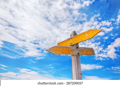 Rustic Yellow Crossroads Sign Against A Cloudy Blue Sky.