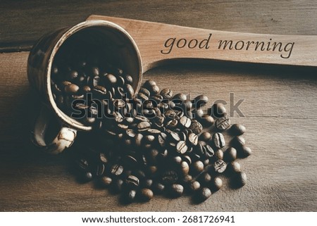 A rustic-style image showcasing roasted coffee beans spilling from an overturned mug onto a wooden surface. A wooden paddle with the words 'Good Morning' adds a welcoming touch. 