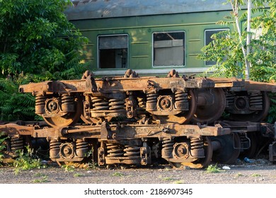 Rusting wagon bogies and old railway equipment from electric locomotives in Tbilisi, Georgia in stock on street on sunny day. Decommissioned soviet engineering put on ground near lush green trees