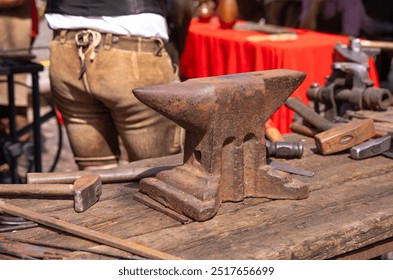 Rusty anvil on a wooden workbench, blacksmith tools spread around in an outdoor workshop setting, traditional metalworking concept - Powered by Shutterstock