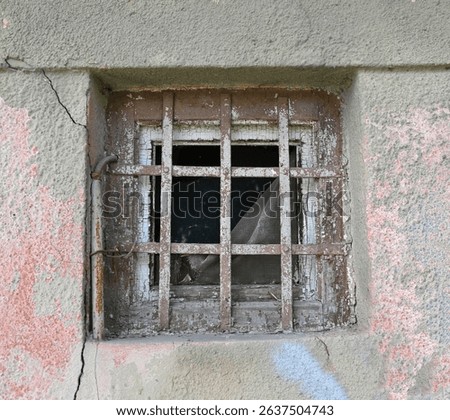 Rusty barred window in a decaying building reveals a dark, neglected space inside. Cracked walls with peeling paint suggest years of abandonment and decay