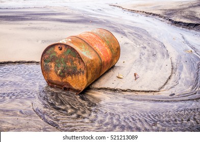 Rusty barrel oil on a partly black coloured beach illustrates the pollution of environment by oil spills