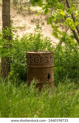A rusty barrel is sitting in a field of grass. The barrel is old and rusted, and it is surrounded by tall grass. The scene is peaceful and quiet, with the only sounds being the rustling of the grass