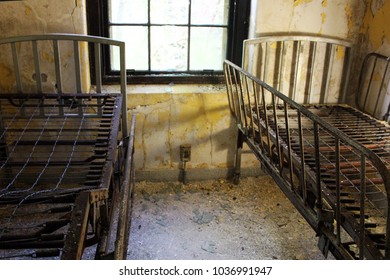 Rusty Bed Frame In Abandoned Mental Asylum Hospital Room With Peeling Paint Walls