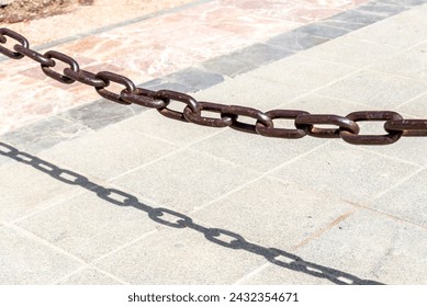Rusty brown chain casting a sharp shadow on sunlit paving stones
