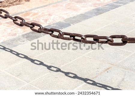 Rusty brown chain casting a sharp shadow on sunlit paving stones