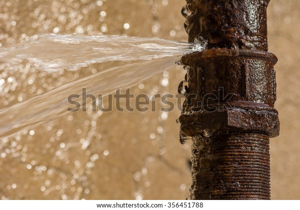 Rusty\
burst pipe spraying water after freezing in\
winter.