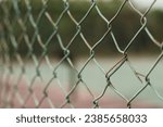 rusty chain link fence with blurry tennis court background. close up view