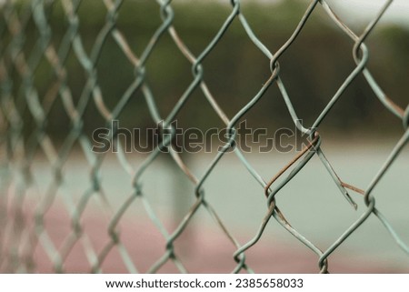 rusty chain link fence with blurry tennis court background. close up view