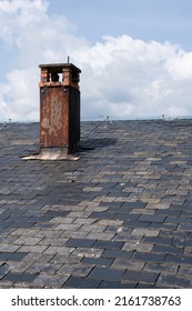 Rusty chimney on a slate roof with a blue cloudy sky