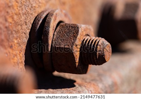 Rusty corroded iron screw with washer and thread on a railway profile in bright sunlight. Monochrome orange brown metal surface of a hex nut fixing. Macro close up with selective focus.