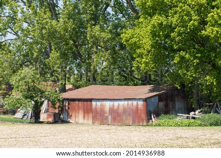 Rusty corrogated iron barn. Storage building in agricultural woodland UK. Old shed structure next to a farm field. Rural England.