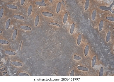 Rusty diamond plate texture background. Close-up top view of a weathered grey metal manhole cover with raised oval anti-slip patterns and heavy iron corrosion for industrial and urban infrastructure concepts.