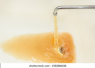 Rusty or dirty water flowing from a tap into a white bathtub or sink