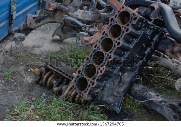 rusty disassembled cylinder block\
on the ground and in the background lies a rusty\
crankshaft