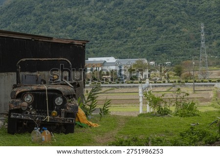 A rusty, extremely dilapidated old banger was abandoned in the countryside of Taiwan. It forms a striking contrast with the lush green mountains and fields in the background.