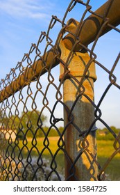 Rusty Fence Post And Chain Link Fence With Blue Sky Background