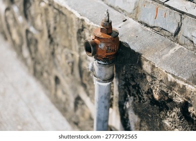 Rusty Fire Hydrant Mounted on Weathered Stone Wall with Metal Pipe and Bolt Details