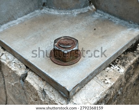 ​Close-up of a rusty hexagonal bolt and nut on a metal plate foundation.

