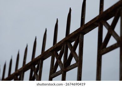 Rusty iron security fence with sharp spikes. Close-up detail of a corroded metal barrier against a gloomy, overcast sky.