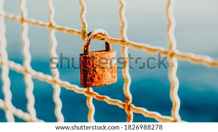 Rusty love padlock hanging on a bridge on a light blue sea background. 16 on 9. Makarska, Croatia
