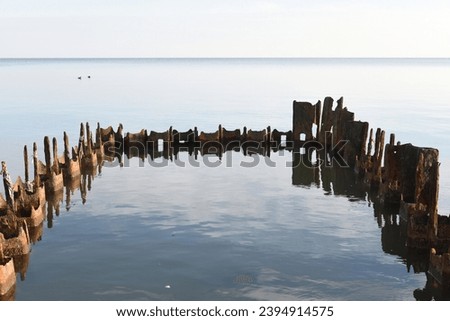 Rusty metal breakwater chain (protective construction) in salt water. Corrosion of hardware in sea water. Light sky reflecting in salt water. January 2022, Mariupol, Central beach, Azov Sea, Ukraine.