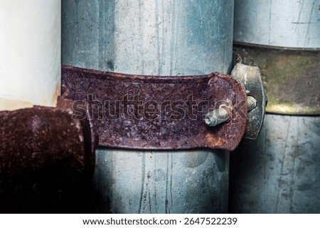 Rusty metal clamp securing galvanized steel pipes together, highlighting the effects of corrosion and the importance of maintenance in industrial settings
