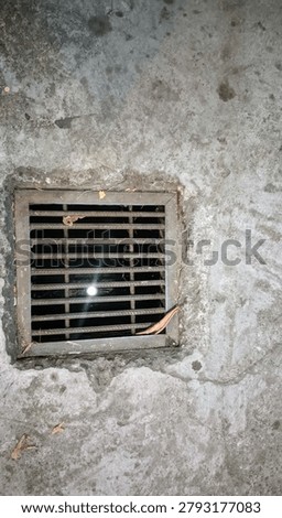 Rusty metal drain grate embedded in weathered concrete wall at night
